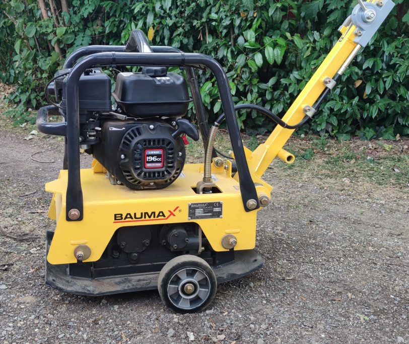 Gelbe Baumaxx Rüttelplatte mit motorisiertem Antrieb, auf einem Schotterweg platziert.