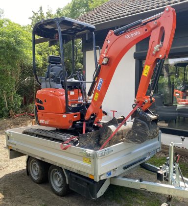 Kompakter Bagger auf einem Anhänger, bereit für den Transport.