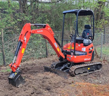 Orangener Minibagger arbeitet im Erdreich, um das Gelände vorzubereiten.