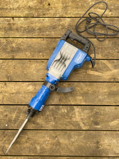 Blauer Abbruchhammer mit Meißel auf Holzboden.