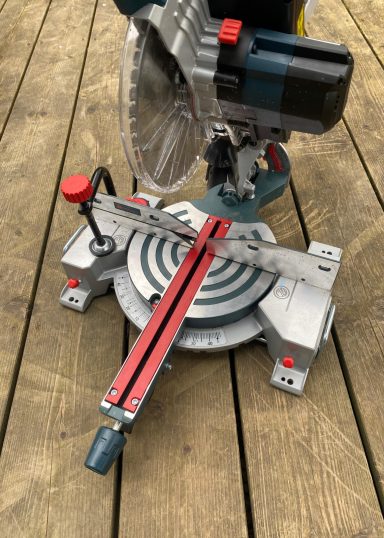 Kapp- und Gehrungssäge mit rotem Handgriff auf einem Holzboden.